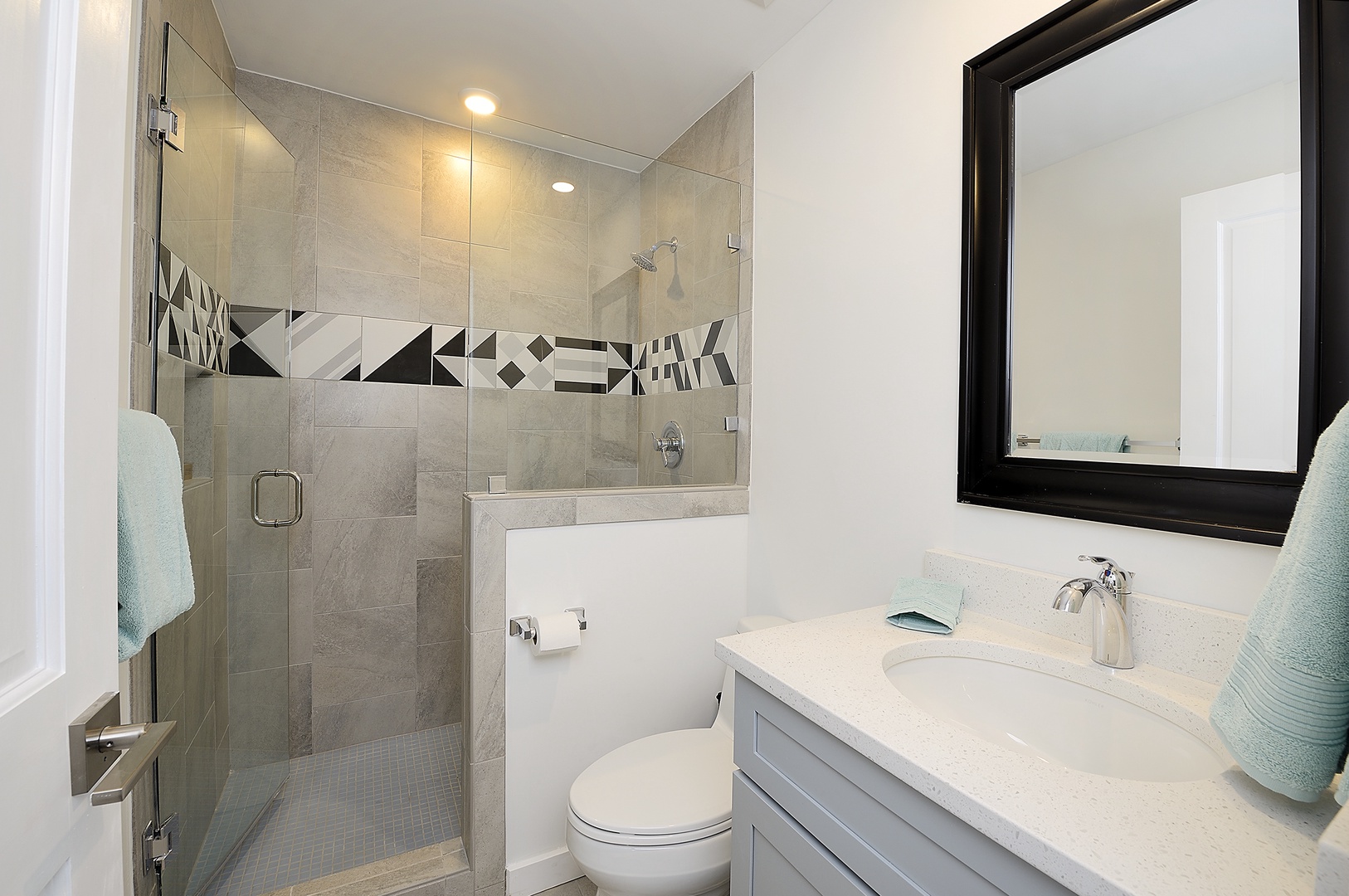 Step into your stylish bathroom with modern glass shower, chic geometric tile accent, and pristine quartz vanity.