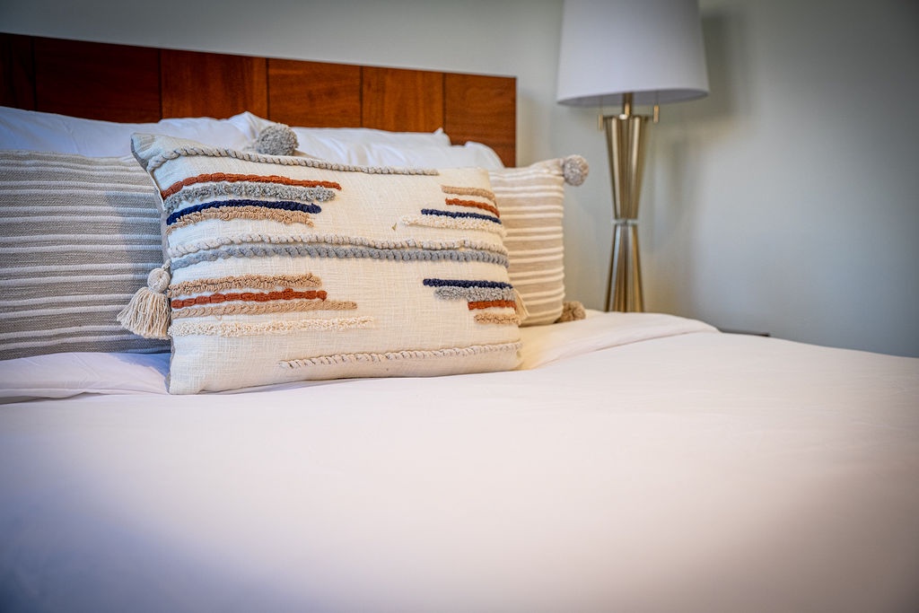 Sink into plush bedding with decorative pillows and warm lighting creating your perfect retreat.