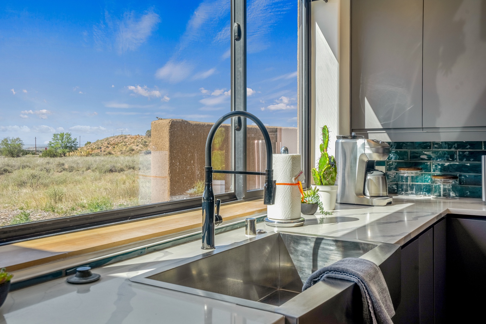 Your sleek kitchen overlooks stunning desert landscapes through floor-to-ceiling windows, creating an inspiring space for cooking.