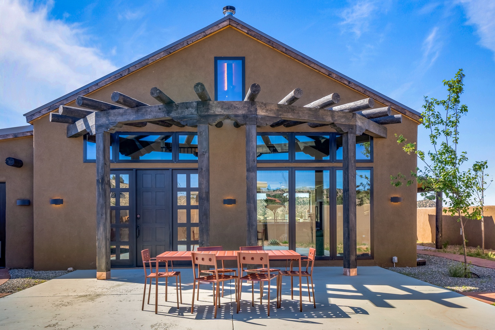 Modern southwestern-style property featuring adobe walls, exposed timber pergola, and large glass windows with desert mountain views.
