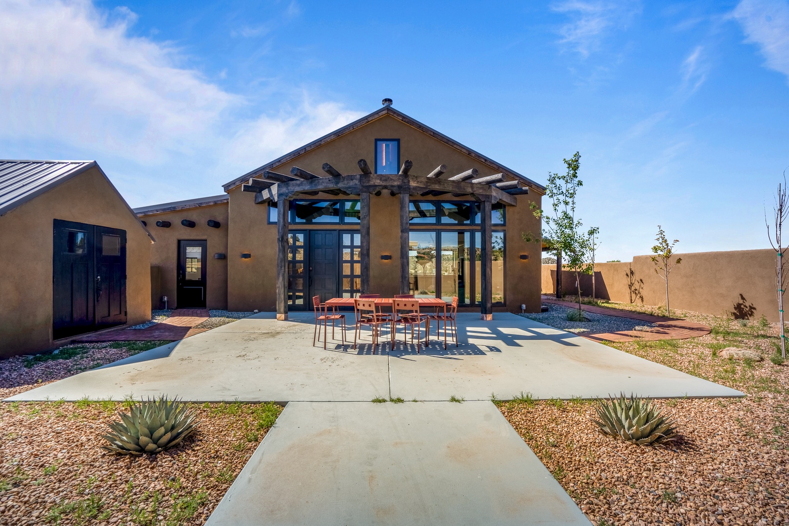 Modern adobe-style property featuring expansive glass doors, covered outdoor dining area, and desert landscaping with mountain views.