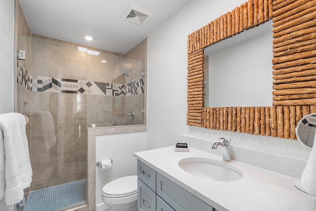 Your private bathroom features a sleek glass shower, modern vanity, and charming driftwood mirror for your coastal getaway.