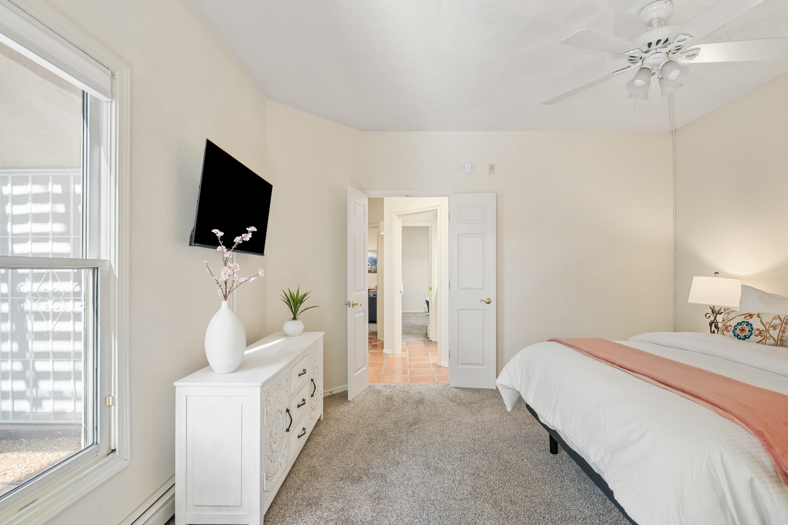 Relax in your bright, airy bedroom featuring a comfortable bed, wall-mounted TV, and stylish décor with plenty of natural light streaming through large windows.