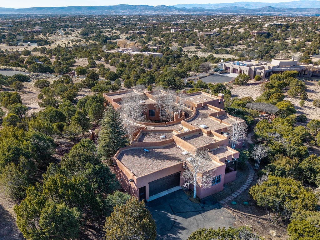 Stunning aerial view showcases this distinctive adobe-style property nestled among mature trees in a peaceful neighborhood with mountain vistas.