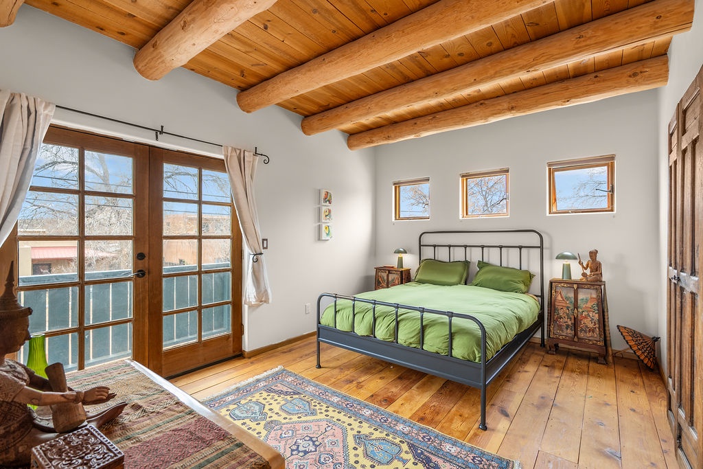 Unwind in your serene bedroom featuring exposed wood beams, vibrant green bedding, and French doors opening to breathtaking views of the surrounding landscape.