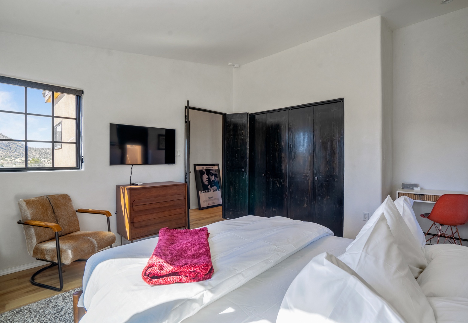 Sink into crisp white linens in your bright, modern bedroom featuring a cozy leather chair and sleek entertainment setup.