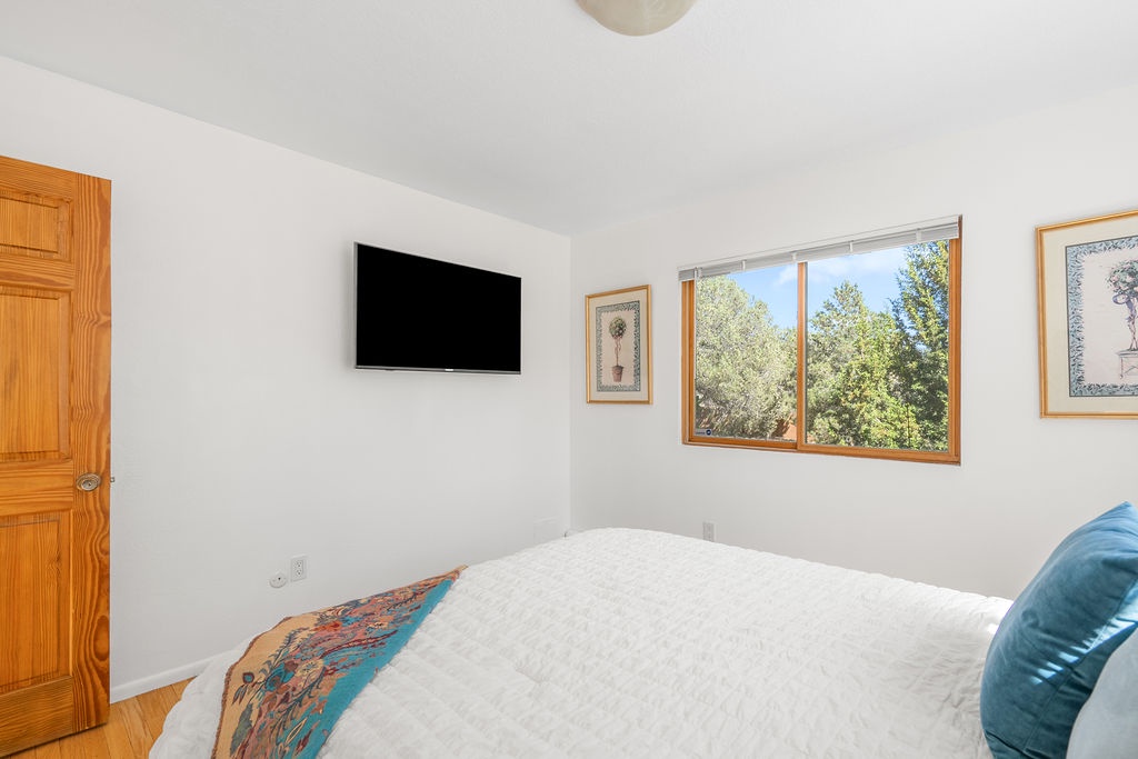 Relax in your peaceful bedroom with crisp linens, wall-mounted TV for entertainment, and a large window framing leafy garden views.