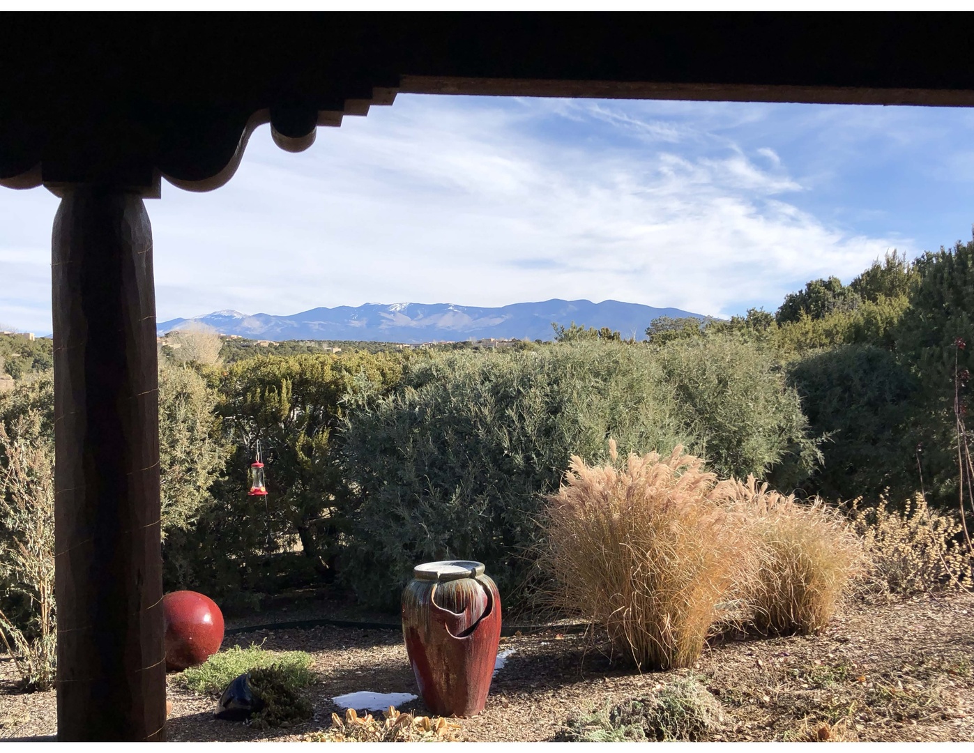 A covered outdoor space overlooks a scenic expanse of high desert vegetation with snow-capped mountain peaks rising in the distance under a partly cloudy sky.