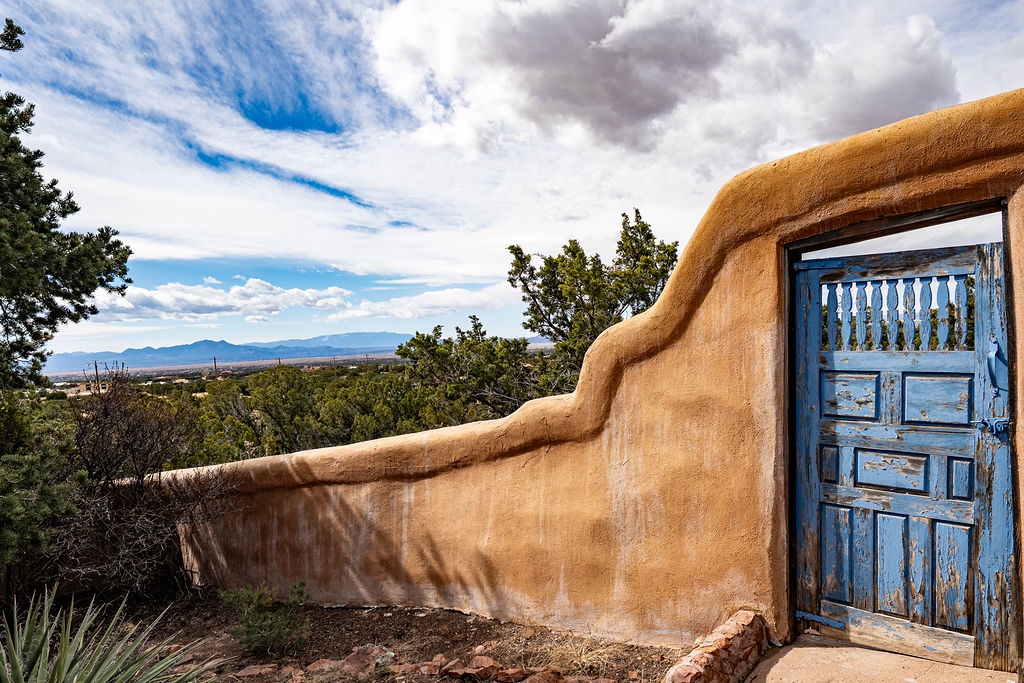Adobe-style architecture with distinctive blue door set against rolling hills and expansive southwestern landscape.