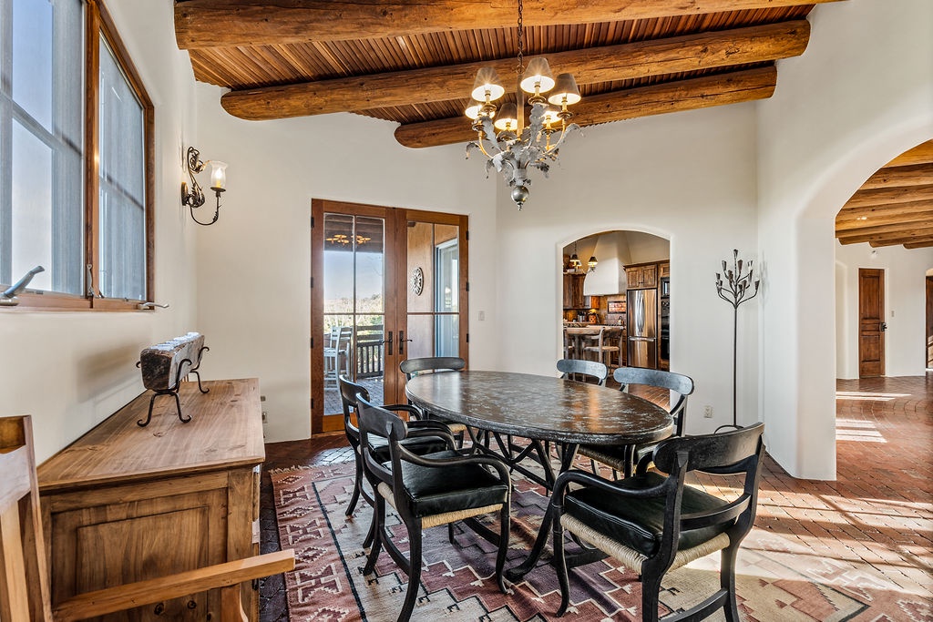Gather around this elegant dining table beneath rustic vigas, where memorable meals unfold under the warm glow of your chandelier.