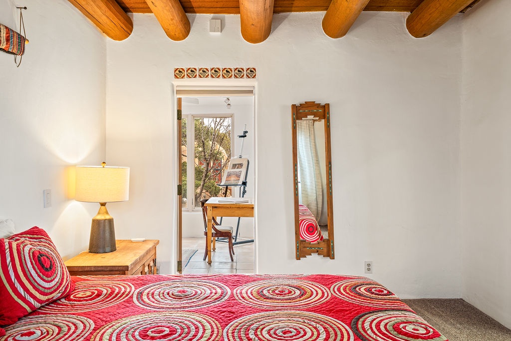 Cozy bedroom with rustic wooden beams and vibrant bedding creates your perfect retreat with workspace nearby.