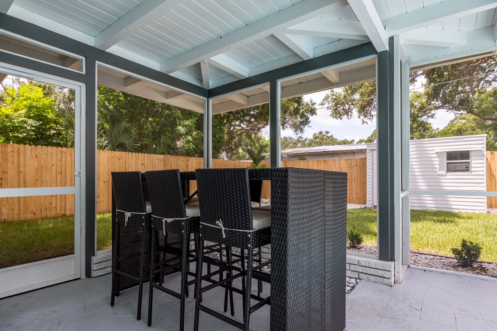 Your covered patio offers perfect outdoor dining with stylish high-top seating surrounded by lush greenery and privacy.