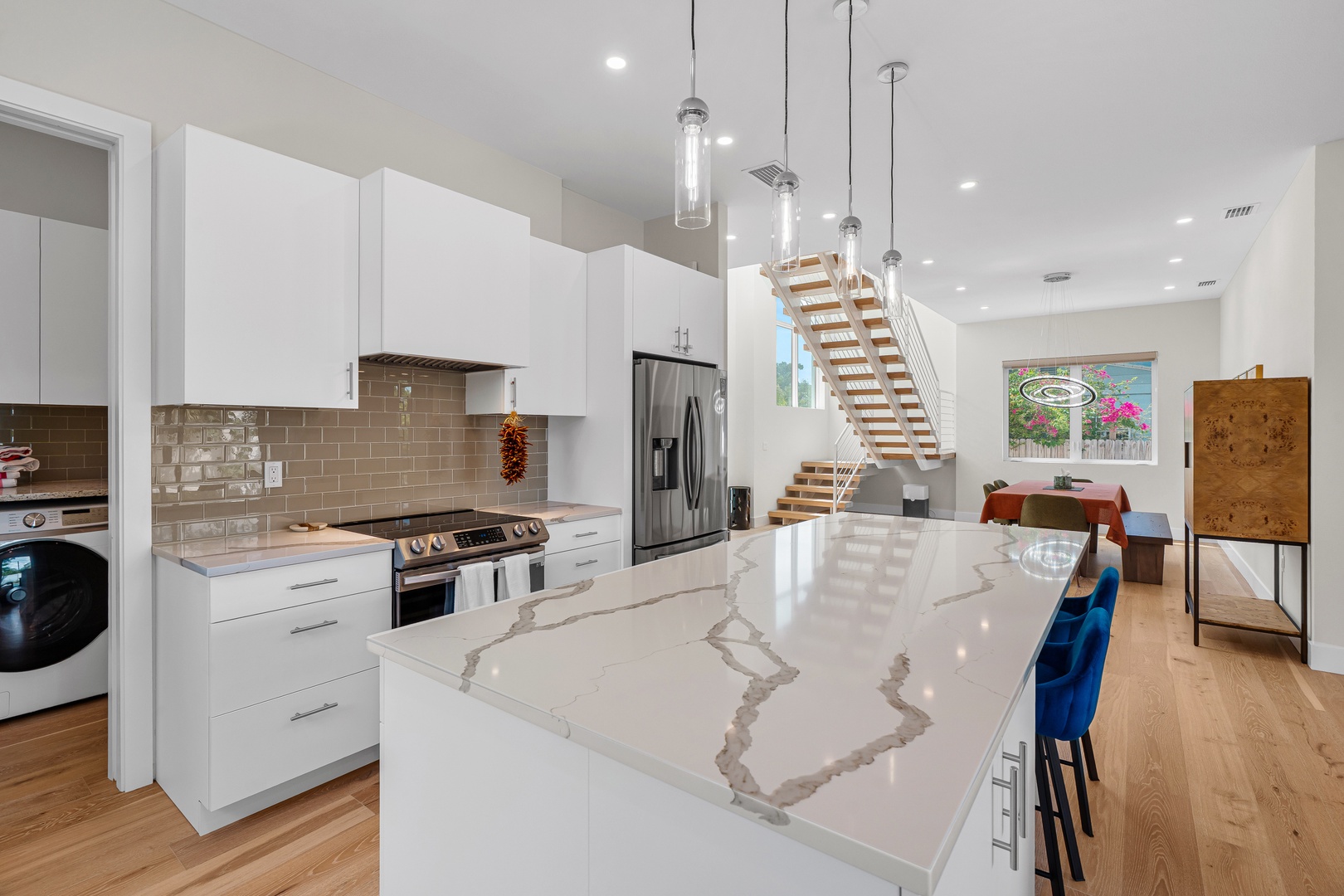 Your fully equipped kitchen gleams with marble countertops and modern appliances, opening seamlessly into an airy living space with soaring ceilings and natural light streaming through every window.