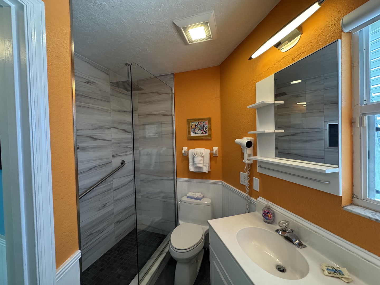 Step into your private bathroom where warm orange tones meet sleek gray tile. Fresh towels await, and the modern walk-in shower promises a refreshing start to your day.