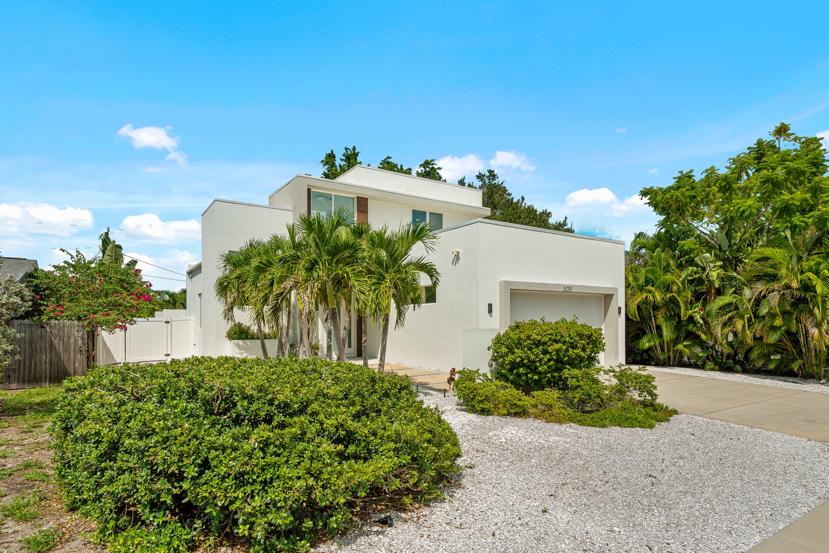 Modern tropical retreat surrounded by lush palms and manicured gardens, nestled in a quiet residential setting with a welcoming driveway entrance.