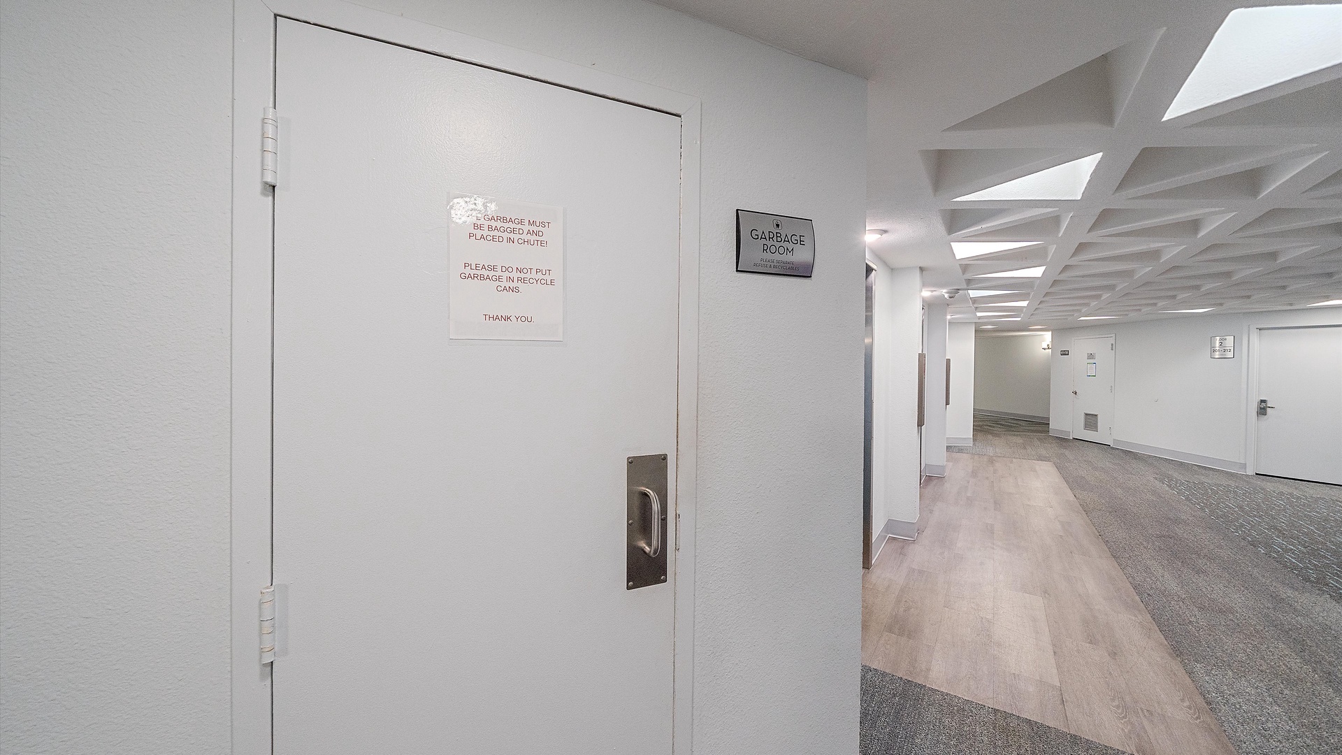 Modern interior hallway with clean white walls and carpeted flooring, featuring utility room access and clear directional signage for easy navigation.