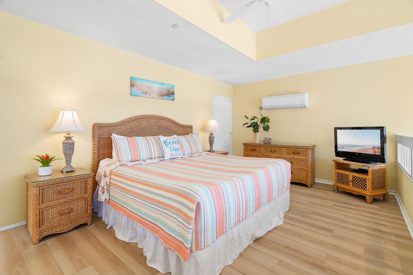 Unwind in your coastal-inspired bedroom, featuring a comfortable bed with cheerful striped linens and warm wicker furnishings for a relaxing beach getaway.