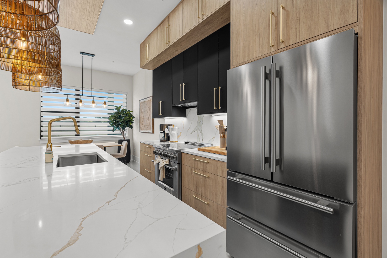 Your chef-worthy kitchen awaits with gleaming stainless appliances, sleek marble counters, and warm wood tones. Ambient woven pendant lights add coastal charm to this perfectly appointed cooking space.