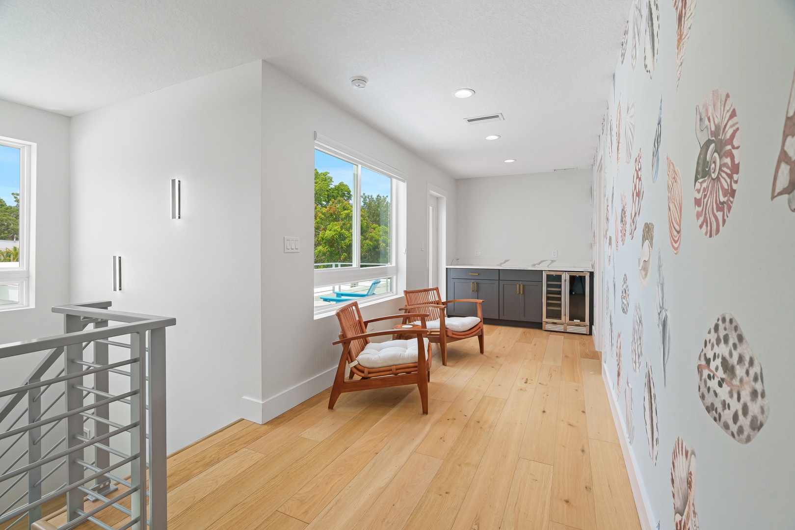 Unwind in your bright upstairs lounge with warm wood floors, stylish seating, a sleek beverage bar, and stunning views of the pool and lush greenery beyond.