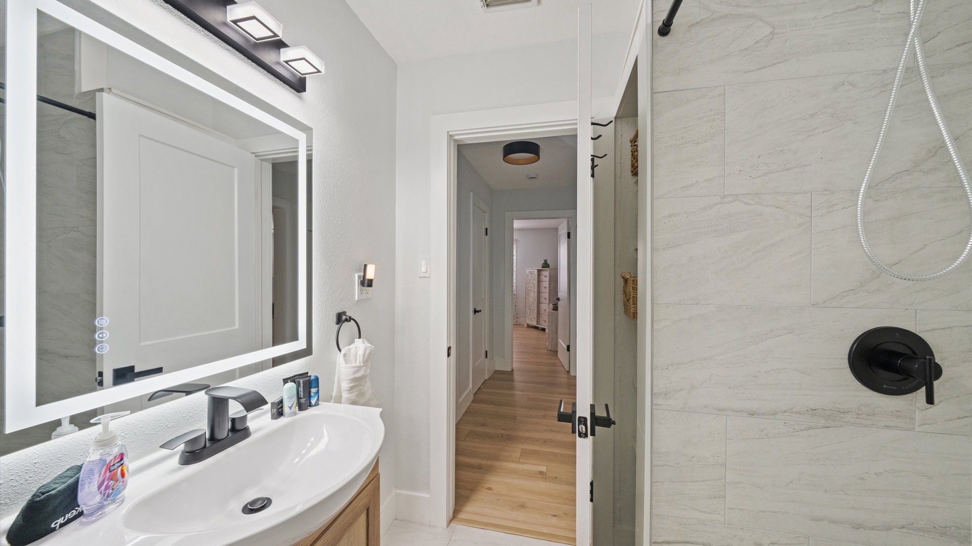 Freshen up in your stylish bathroom with modern fixtures, a bright LED mirror, and a sleek walk-in shower with elegant stone-look tile.