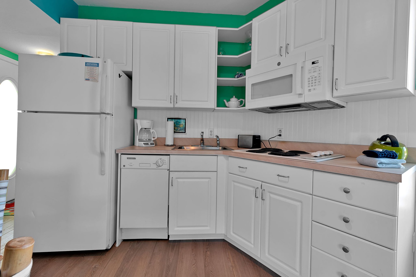 Your vacation rental kitchen features bright white cabinetry, modern appliances, and a cheerful pop of teal, giving you everything you need to prepare meals comfortably during your stay.