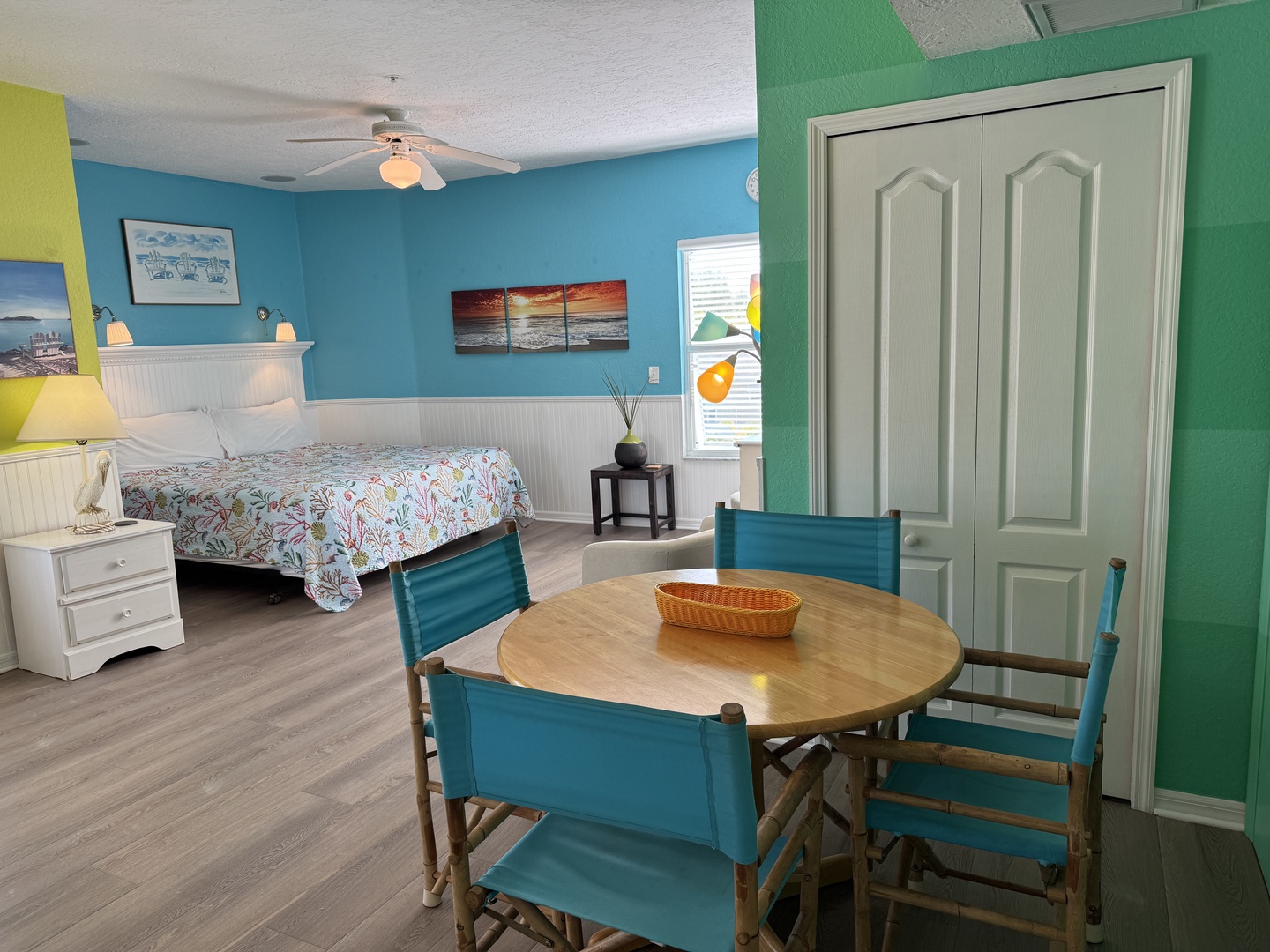 Your colorful beach retreat awaits with a cozy bed dressed in tropical linens, a charming dining table for meals and games, and vibrant walls that capture the coastal spirit.