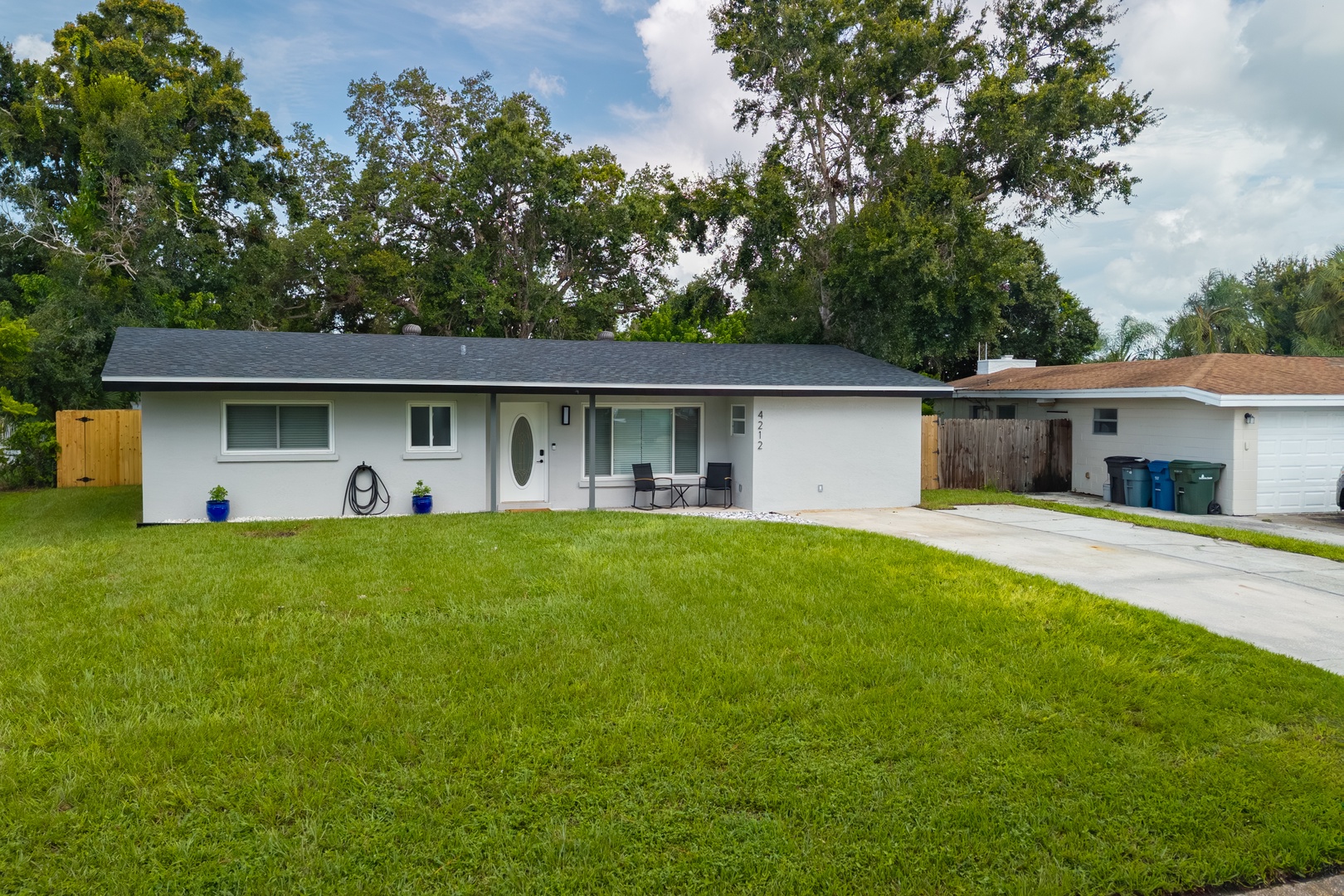 A charming single-story home with a spacious front lawn, covered porch seating area, and convenient driveway parking in a peaceful residential neighborhood.