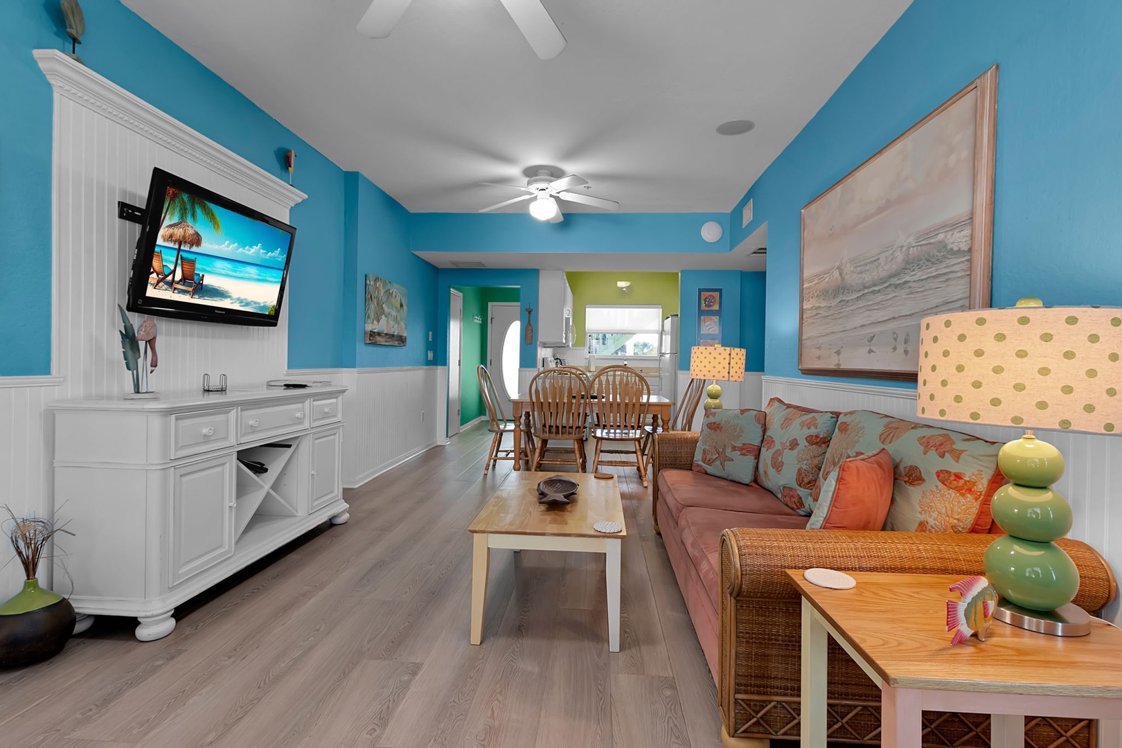 Relax in your bright coastal living space with comfortable seating, ceiling fan, and cheerful beach-inspired decor. The open layout flows seamlessly to your dining area and kitchen beyond, perfect for gathering.