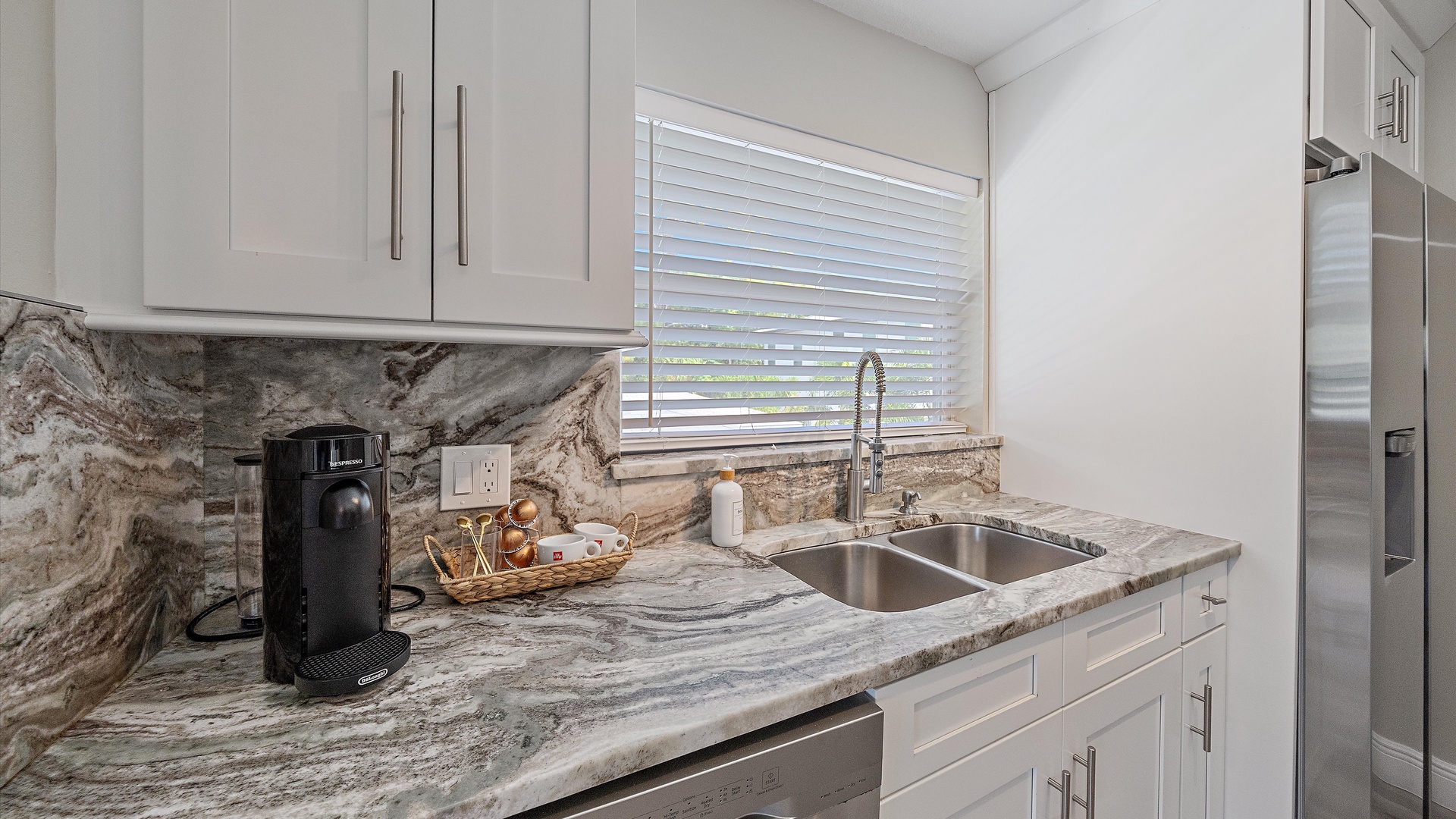 Settle in and brew your morning coffee in this sleek, sun-filled kitchen. Natural light streams through the window, casting a warm glow over the marble countertops and modern appliances—ready for your vacation meals.