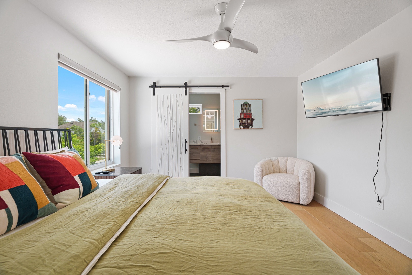 Your bright, modern retreat features a plush king bed and cozy seating nook, with garden views and en-suite bathroom access. Enjoy the gentle breeze from the ceiling fan as you unwind.