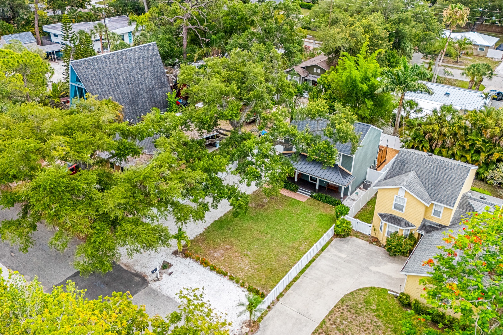 An aerial view showcasing the property nestled in a lush, tree-lined residential neighborhood with nearby homes and tropical landscaping.