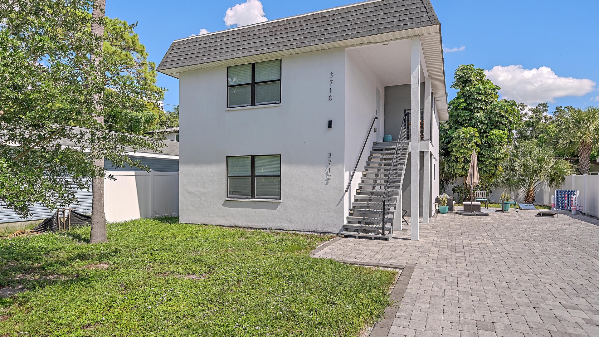 A modern two-story vacation rental with private outdoor entrance, paver walkway, and inviting backyard space framed by lush tropical trees—your Florida escape awaits.