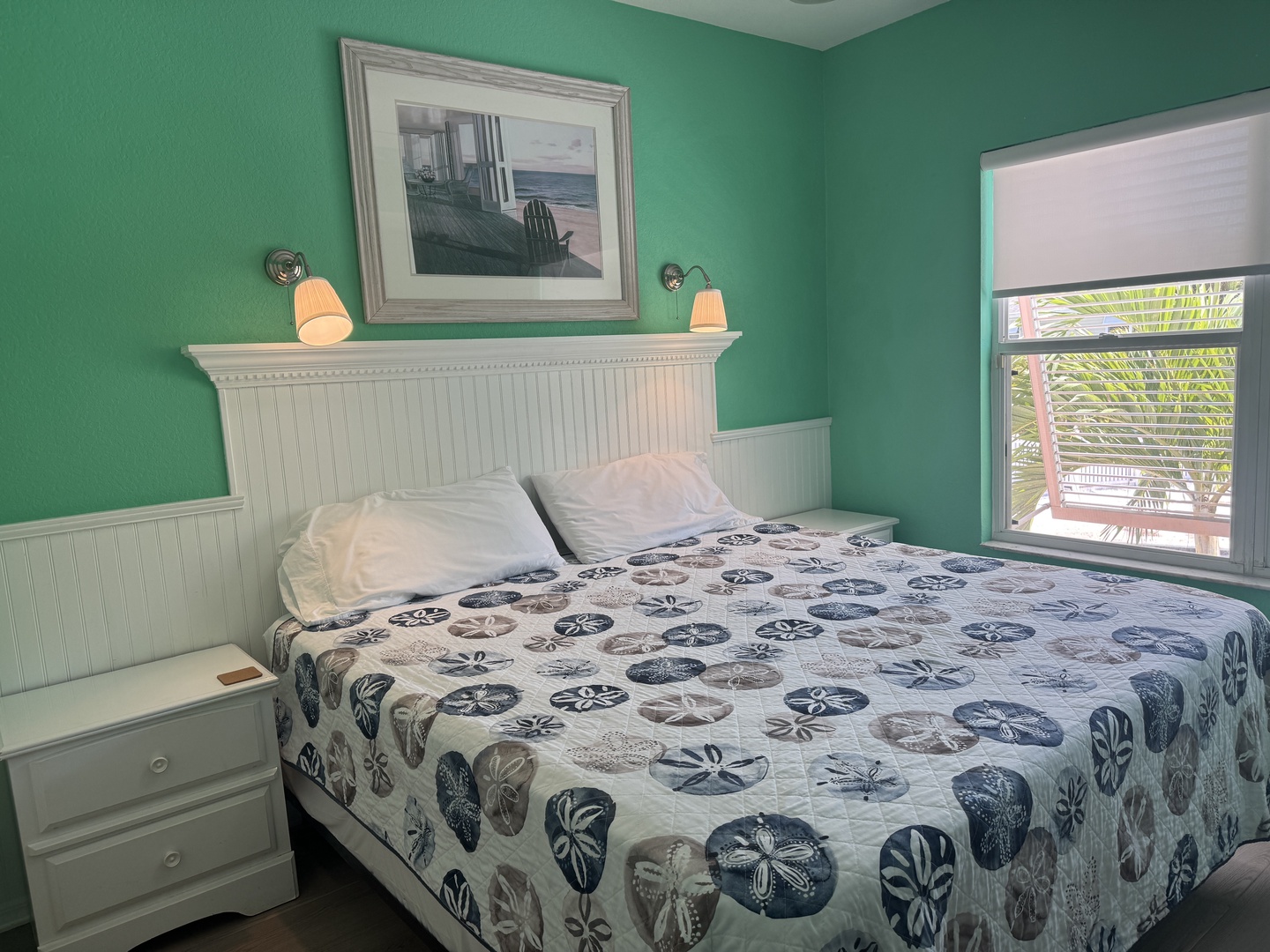 Sink into coastal comfort beneath soft turquoise walls and crisp white linens. Your window frames tropical palms and peaceful views, while gentle sconces create a soothing glow for restful evenings.