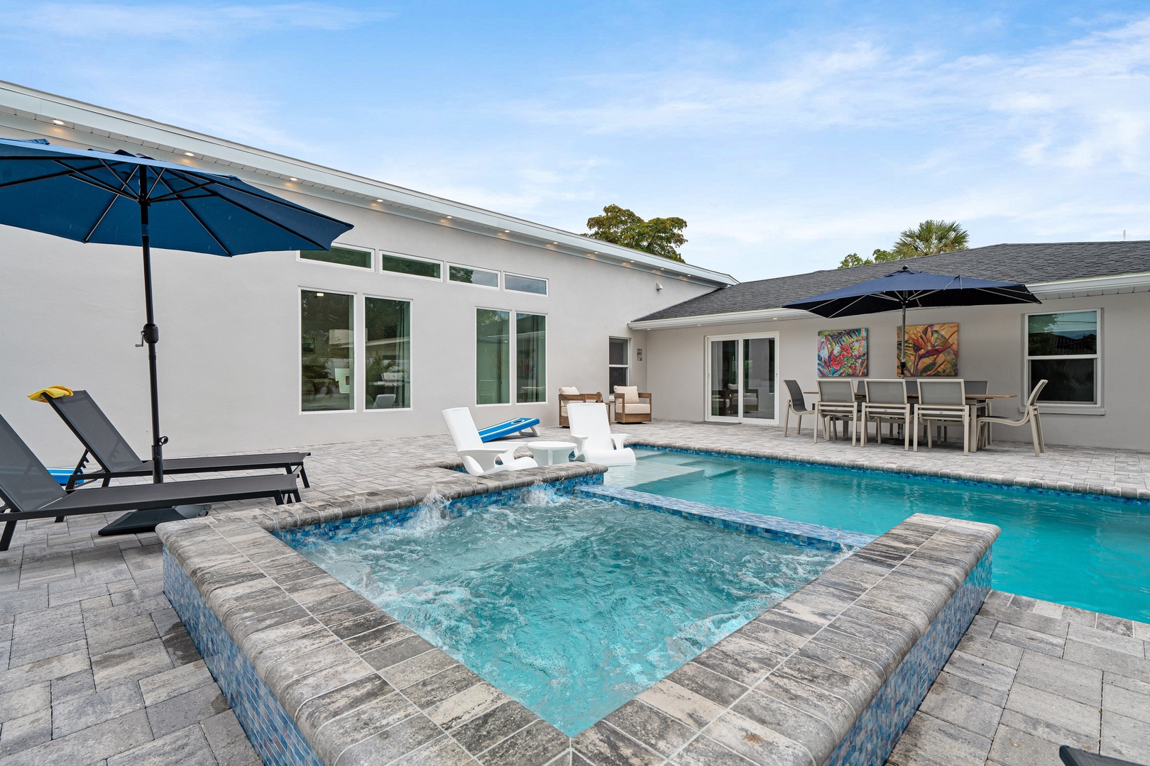 Lounge poolside in the private backyard oasis. Spacious paver deck, refreshing pool and spa, and covered dining create the perfect setting for relaxation and outdoor entertaining under sunny skies.