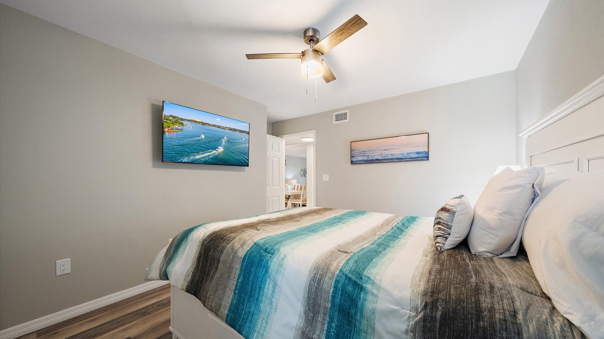 Drift off in this coastal-inspired guest bedroom with soft teal and sand-toned bedding, ceiling fan, and serene lighting. Your peaceful retreat awaits.