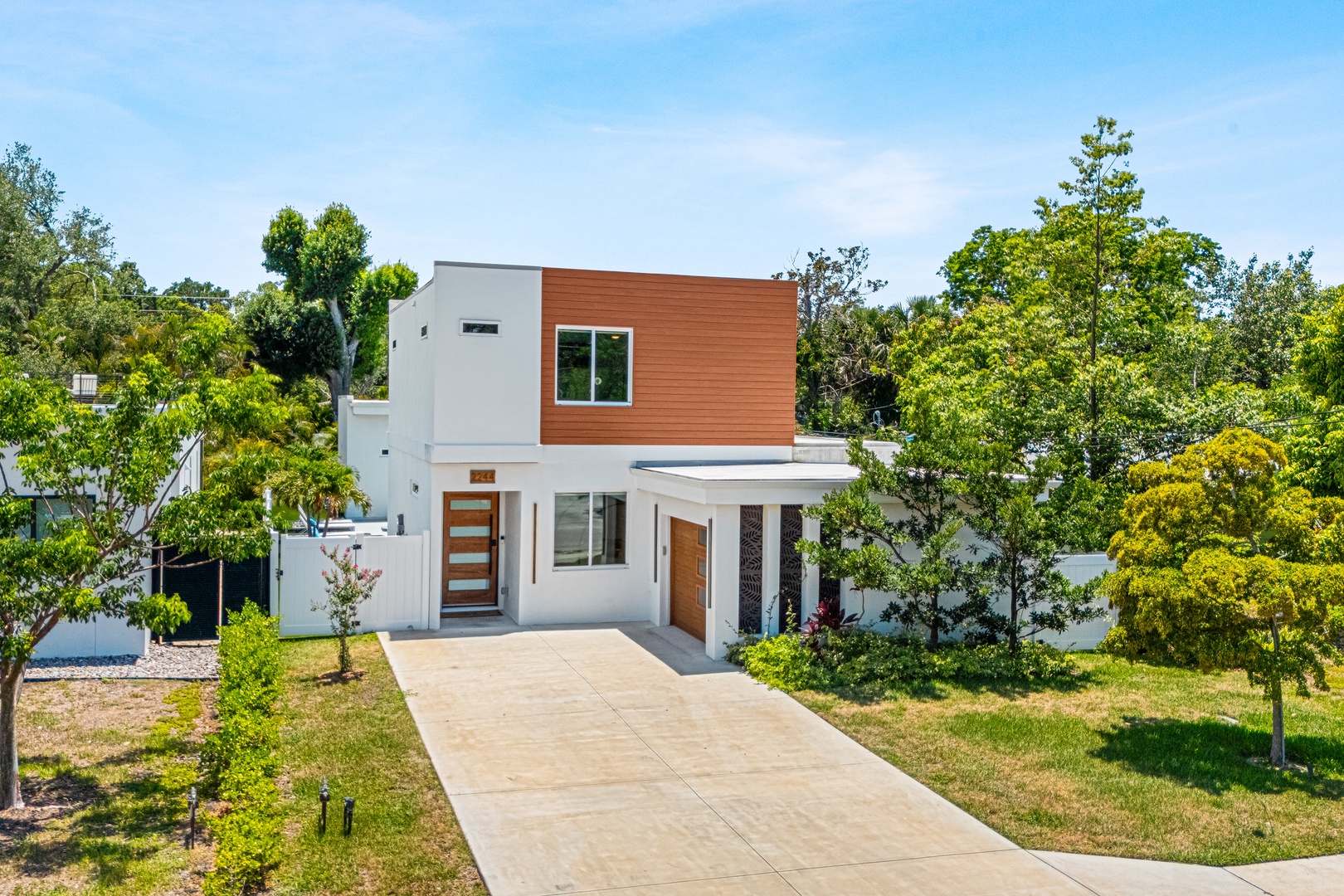 Modern two-story home with warm wood accents, nestled in a leafy residential neighborhood. The clean-lined architecture and private driveway mark the arrival point.