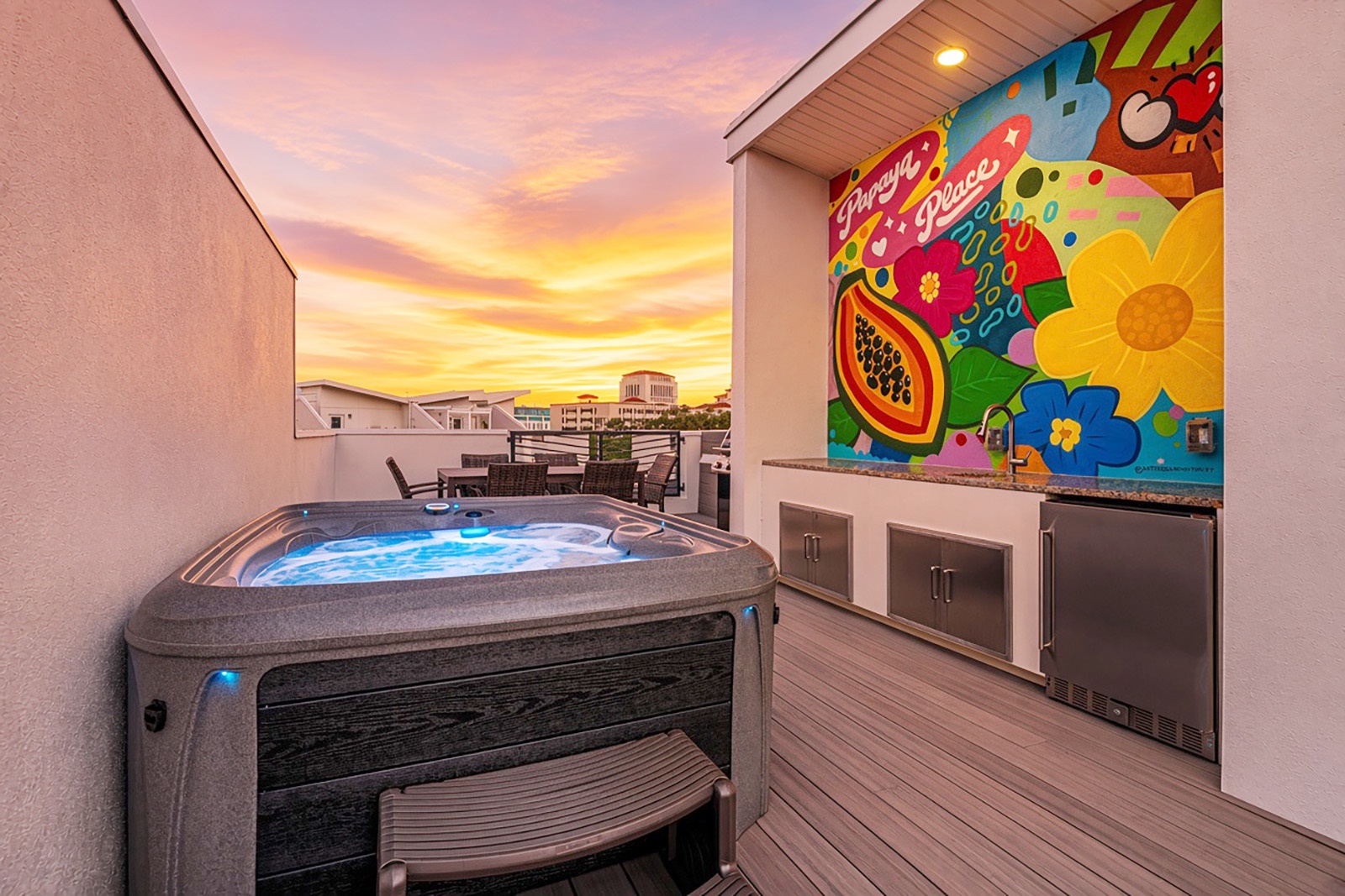 The rooftop terrace with hot tub and vivid tropical mural captures a stunning sunset over the surrounding area.