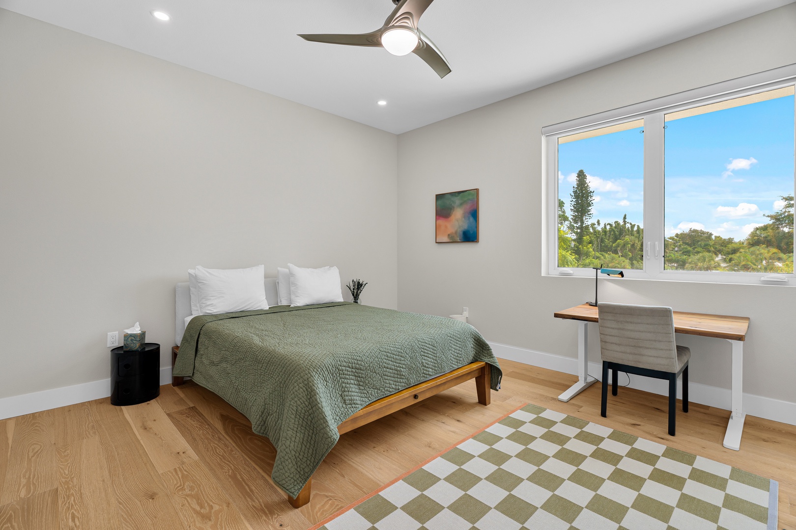 Rest easy in your light-filled bedroom with a comfy bed, desk workspace, and ceiling fan to keep you cool while you take in views of blue skies and greenery through the windows.