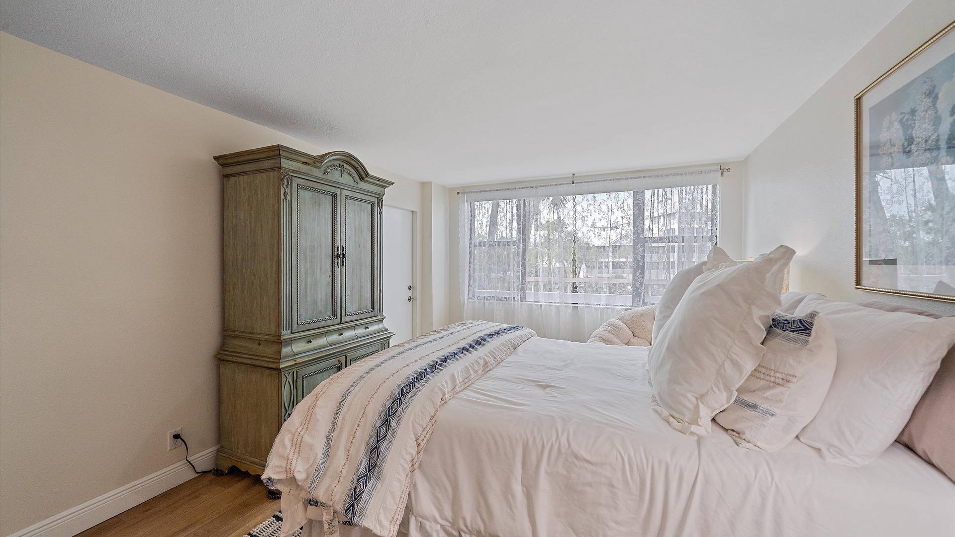 Relax in your comfortable bedroom featuring a plush bed with crisp white linens, elegant wardrobe storage, and bright natural light from large windows.