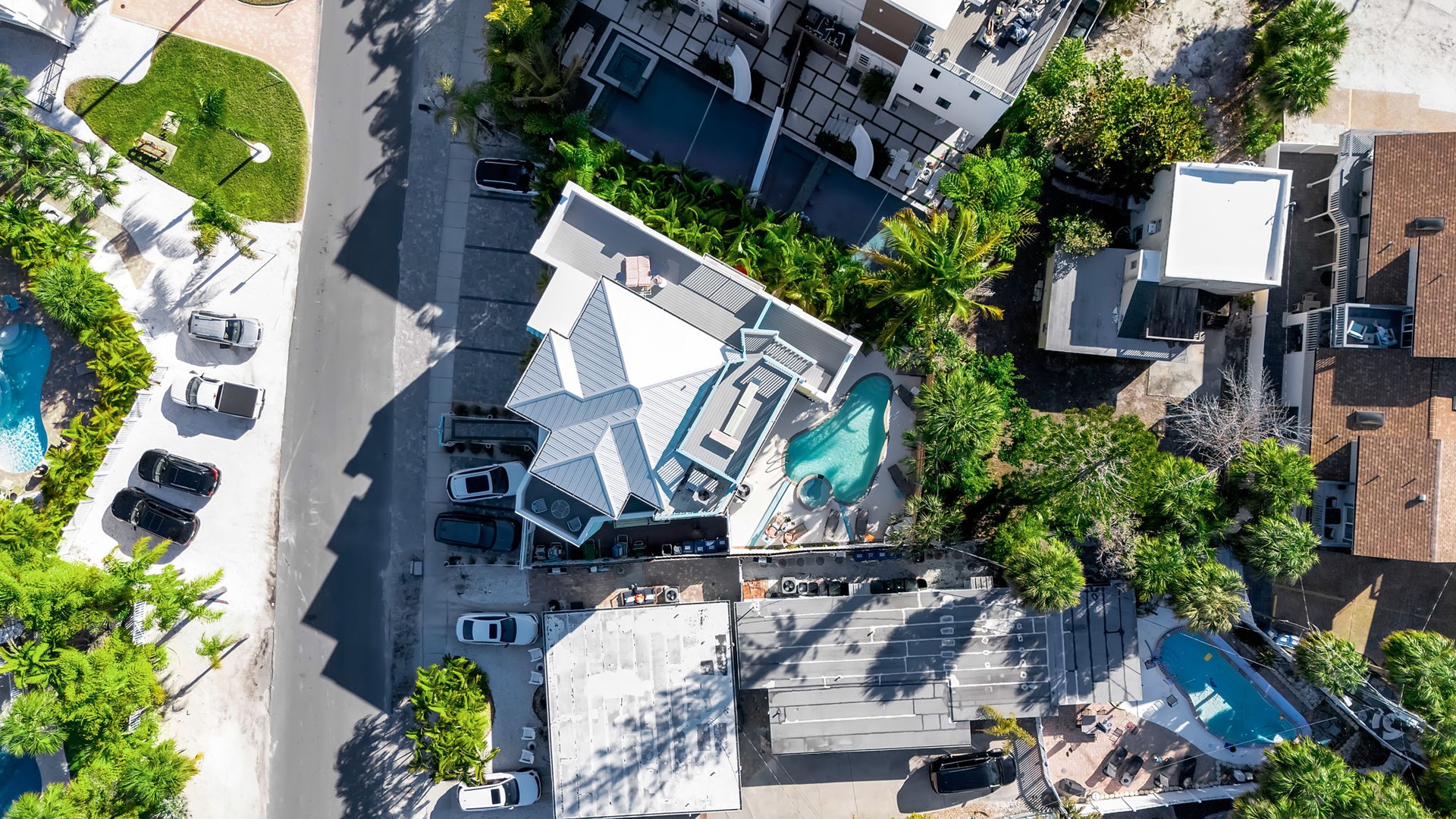 Aerial view of a modern property nestled in a tree-lined residential neighborhood with swimming pools, parking areas, and contemporary rooftops.