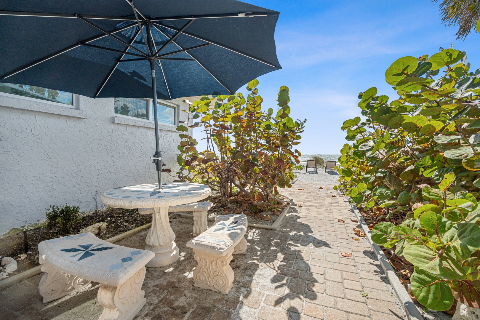 Charming patio with ornate table, umbrella shade, and lush tropical plants creates your perfect outdoor retreat. Charcoal grill provided.