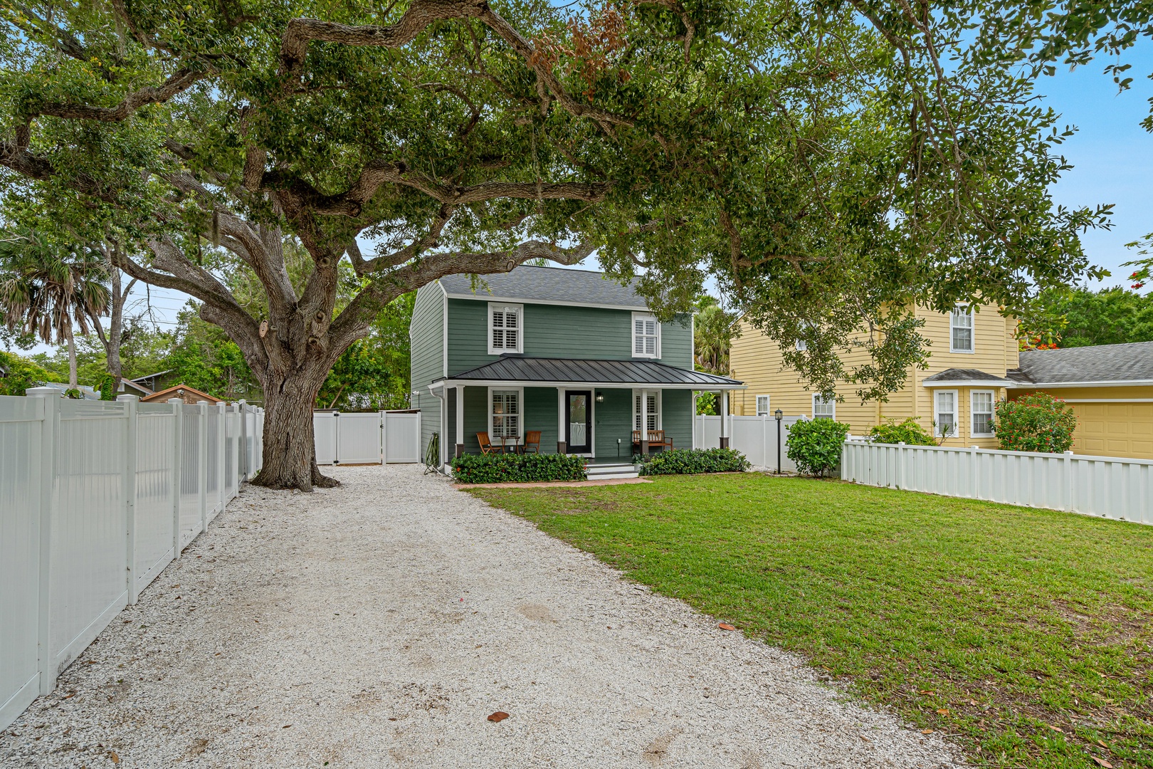 A charming two-story rental home with a welcoming front porch, shaded by a majestic oak tree and surrounded by lush greenery in a peaceful neighborhood.