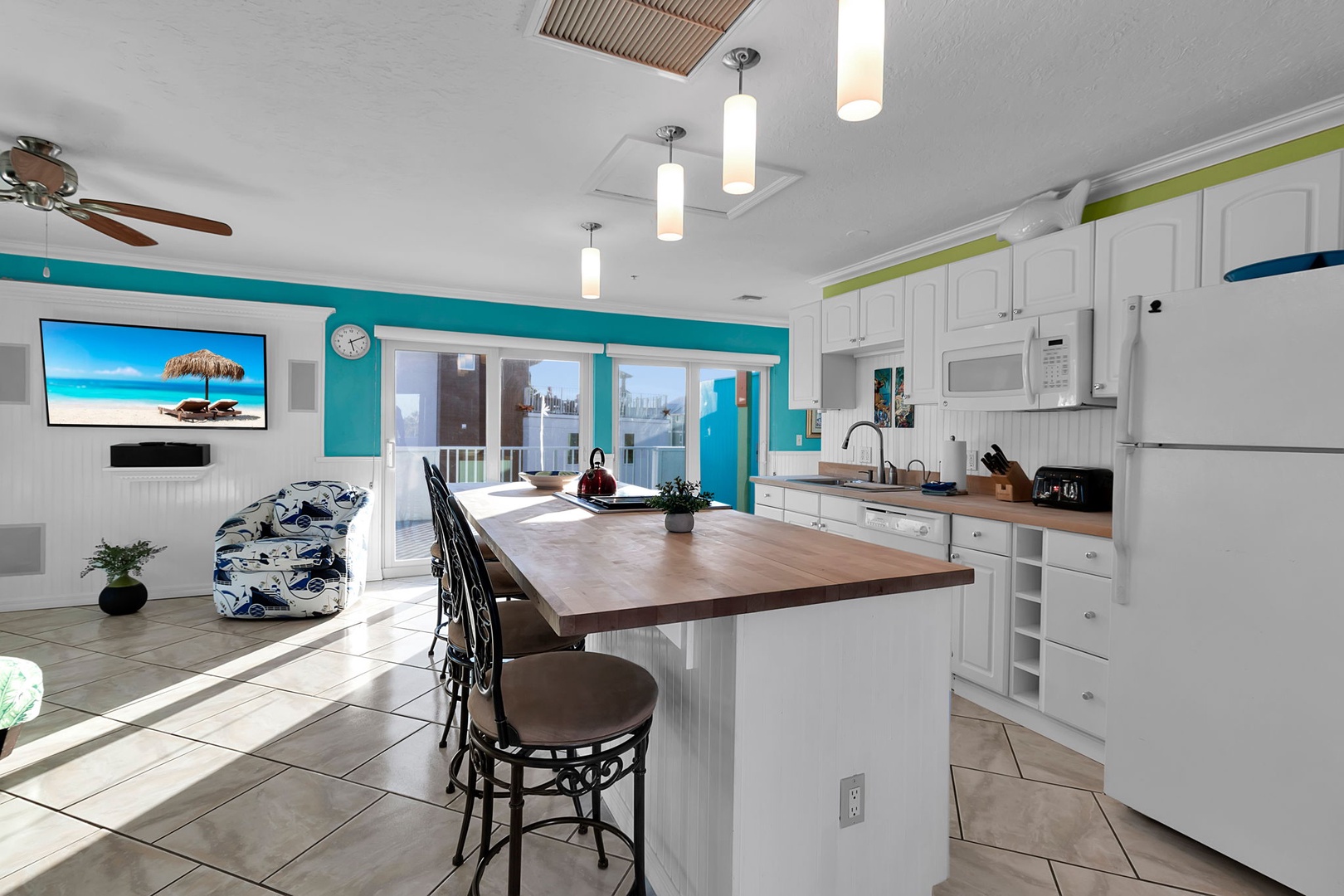 Bright, open living space where you can gather around the central island, cook your favorite meals, and relax in coastal-inspired comfort with vibrant turquoise accents and sunlit views beyond the patio doors.