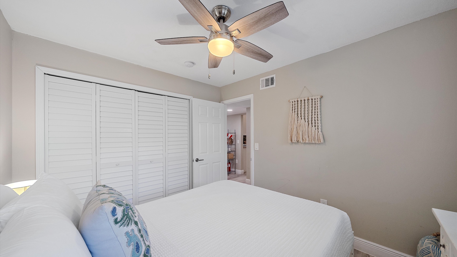 Drift off in your serene bedroom featuring a crisp white bed, calming coastal tones, and a ceiling fan to keep you cool and comfortable throughout your stay.