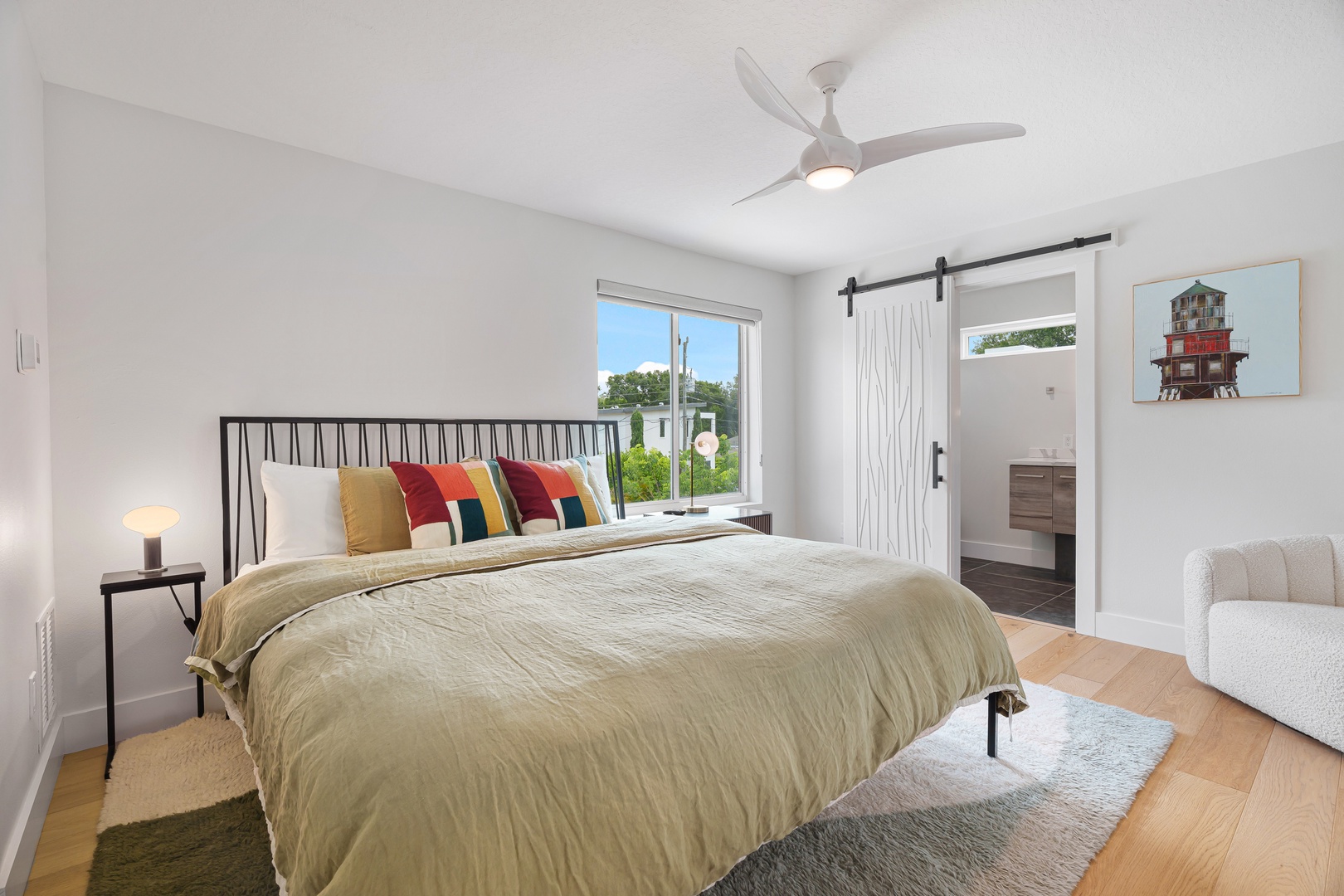 Drift into tranquil sleep in this bright, airy bedroom with coastal-inspired decor, a plush bed, and gentle ceiling fan breeze. Your private ensuite awaits just beyond the charming barn door.