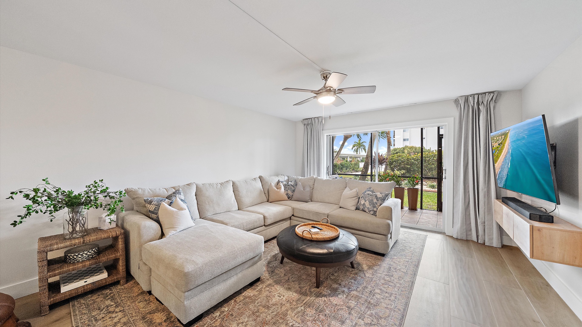 Sink into your spacious sectional sofa while enjoying tropical garden views through floor-to-ceiling windows in this bright, airy living room.