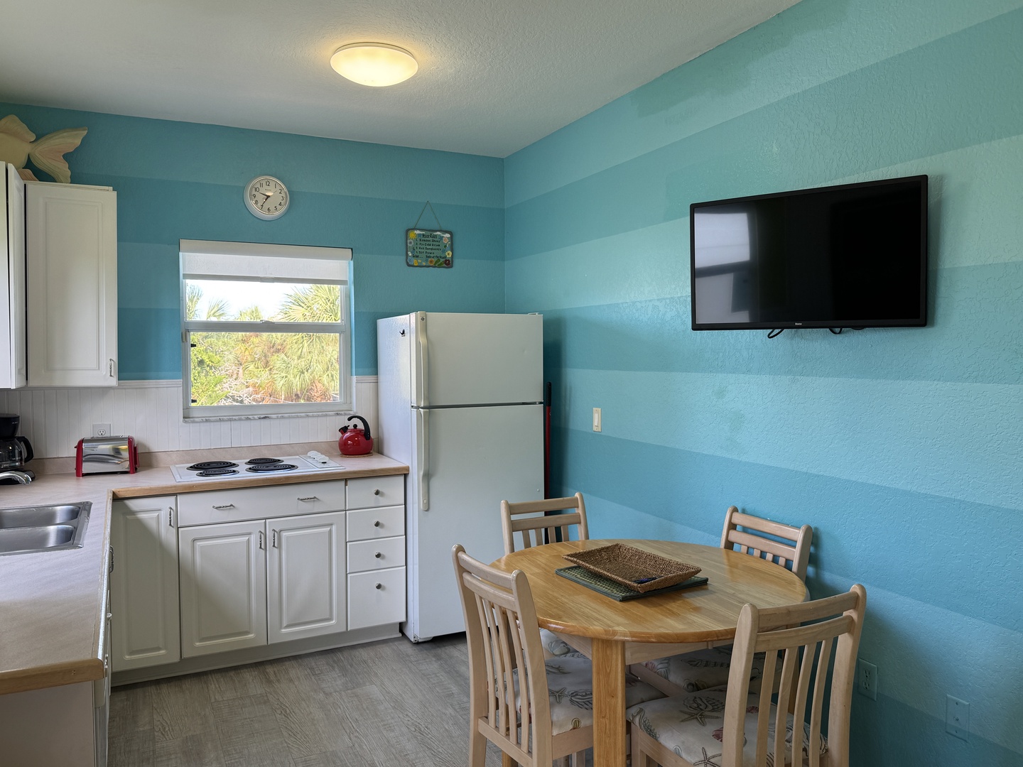 Cook your favorite meals in this bright, beach-inspired kitchen with everything you need for a comfortable stay. The cheerful turquoise walls and natural light through the window create a relaxing coastal atmosphere for your getaway.