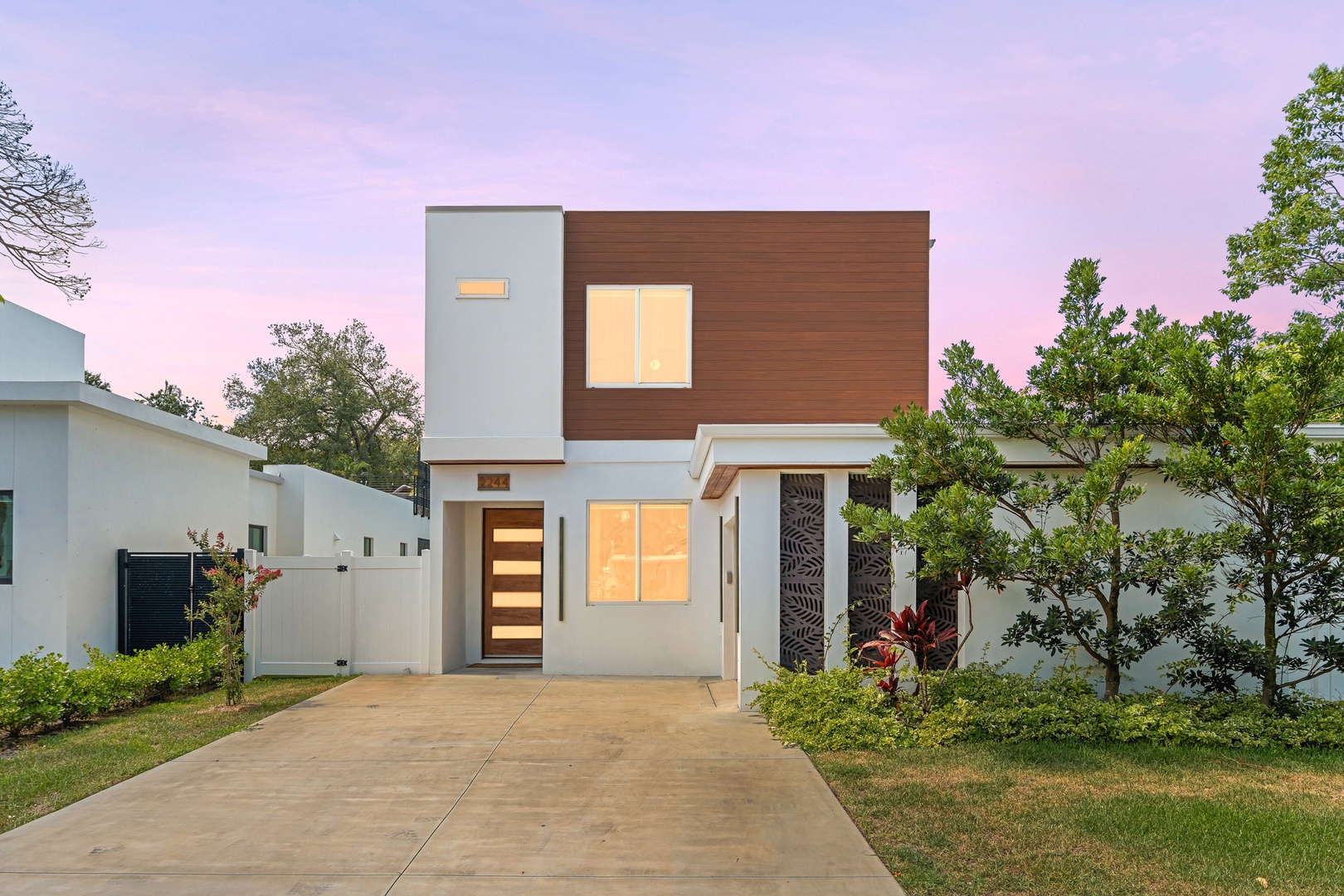 Modern two-story home featuring a striking wood and white exterior with landscaped greenery, set against a tranquil twilight sky.