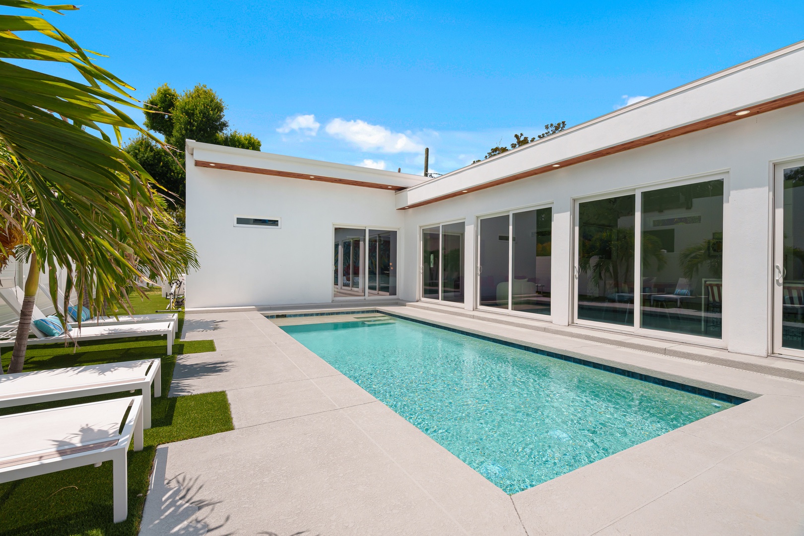 This modern property features a sleek private pool framed by clean white architecture and tropical palms, creating an inviting outdoor retreat under clear blue skies.