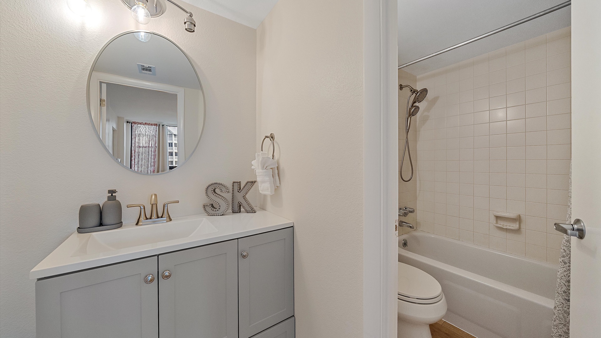 Step into your modern, well-appointed bathroom with a spacious vanity, round mirror, and relaxing tub-shower combo for your comfort and convenience.